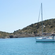 Sailboat anchored in a serene bay with clear blue water and lush green hills under a bright, sunny sky.