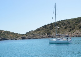 Sailboat anchored in a serene bay with clear blue water and lush green hills under a bright, sunny sky.