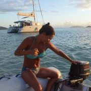 Woman starting a boat motor on the ocean, with a catamaran anchored nearby at sunset. Perfect for powerboating adventures.