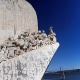 Stone monument with explorers overlooking a deep blue river, perfect backdrop for a Lisbon powerboating adventure.