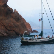 Sailboat anchored near rocky shoreline with two people on board, enjoying the serene coastal view.