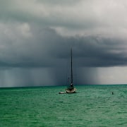 Sailboat in a calm sea facing an approaching storm on the horizon, capturing the power of nature on the open water.