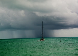 Sailboat in a calm sea facing an approaching storm on the horizon, capturing the power of nature on the open water.