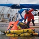 Man in red suit stepping onto a liferaft from a sailboat named Little Wing on calm waters.