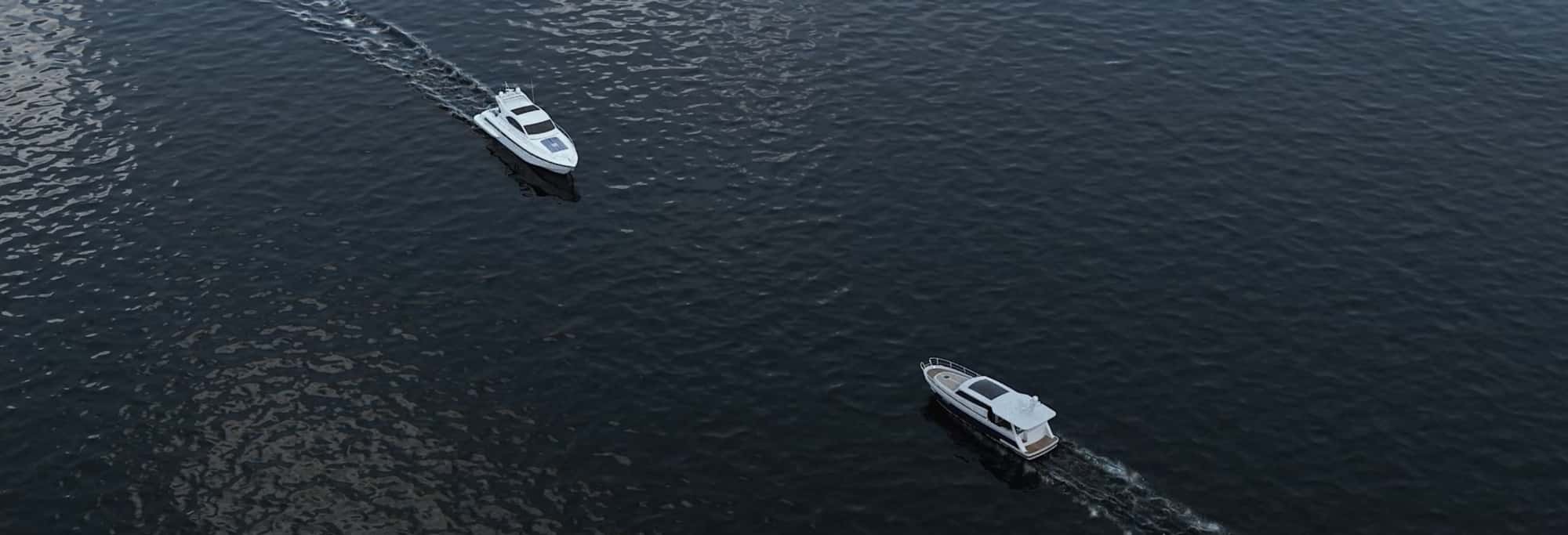 Two powerboats cruising on a calm, open water surface, creating gentle ripples under a clear sky.