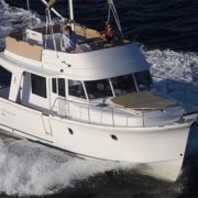 White motor yacht cruising at high speed on open water, with two people on deck enjoying the ride.