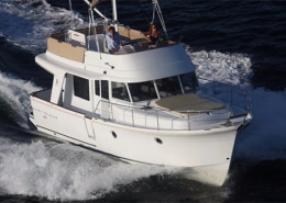 White motor yacht cruising at high speed on open water, with two people on deck enjoying the ride.