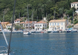 Tranquil marina with moored sailboats in front of colorful seaside village, framed by lush greenery and clear blue waters.