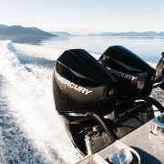 Twin Mercury outboard engines powering a speedboat across a serene lake with scenic mountain views.