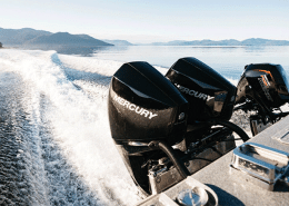 Twin Mercury outboard engines powering a speedboat across a serene lake with scenic mountain views.