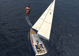 Aerial view of a powerboat towing a sailboat on the ocean.