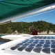 Person navigating a powerboat with solar panels, surrounded by blue waters and lush green coastline.