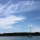 Sailboat gliding on tranquil waters under a bright, cloud-filled sky near a lush, green shoreline. Perfect day for boating.