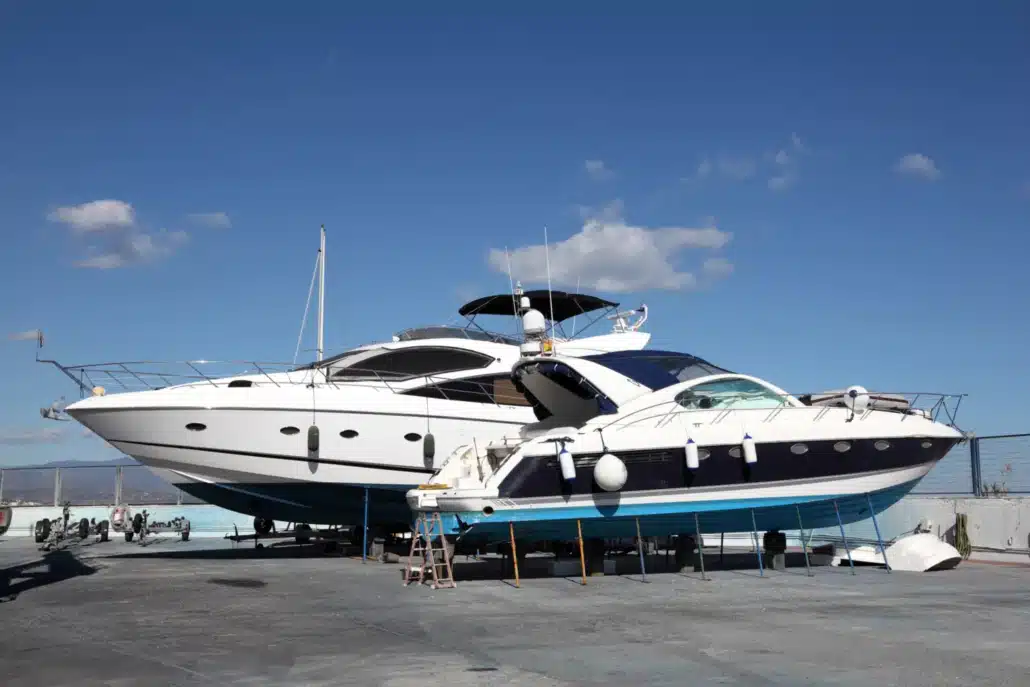 Two luxury powerboats on dry dock under a clear blue sky, showcasing repairing powerboats.