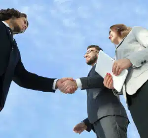 Business meeting handshake under blue sky, signifying partnership and collaboration.