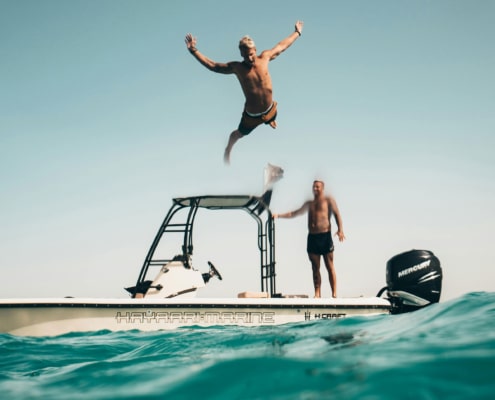 Man jumps into ocean from center console powerboat on sunny day, embracing adventure and freedom.