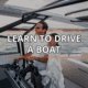 A couple learning to drive a powerboat on the water at sunset, featuring Learn to Drive a Boat text overlay.