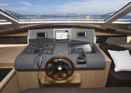 Luxury powerboat cockpit with navigation screens, polished wood steering wheel, and ocean view under clear skies. is driving a yacht hard