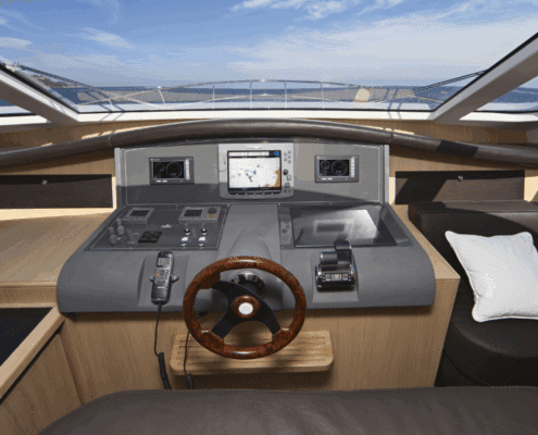 Luxury powerboat cockpit with navigation screens, polished wood steering wheel, and ocean view under clear skies. is driving a yacht hard