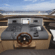 Luxury powerboat cockpit with navigation screens, polished wood steering wheel, and ocean view under clear skies. is driving a yacht hard