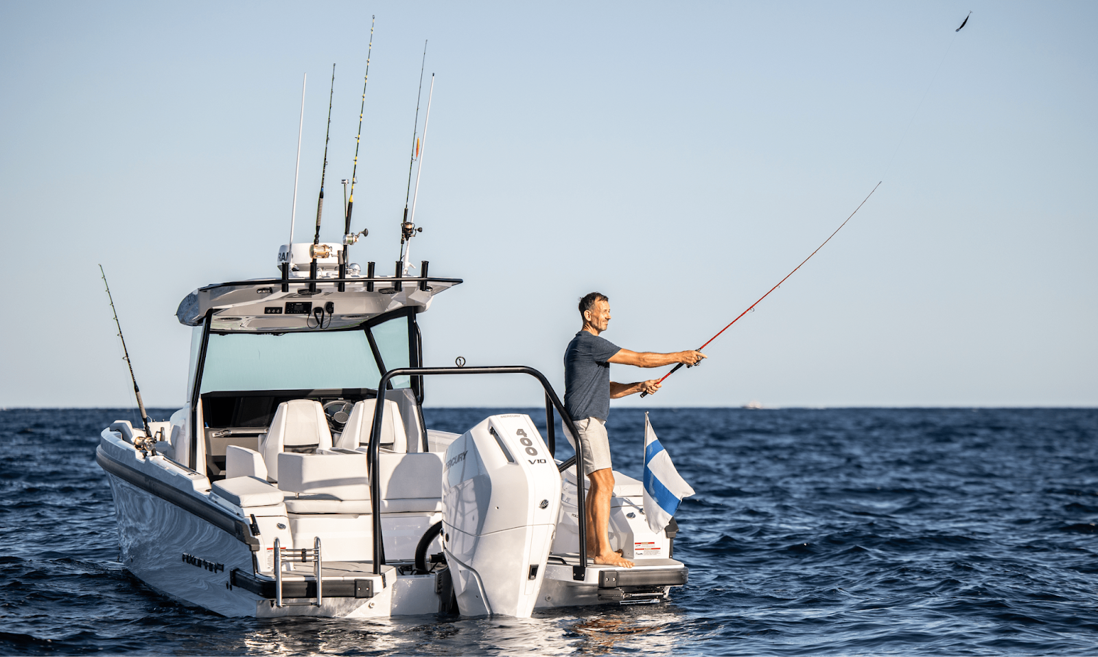 Man fishing on powerboat at sea, enjoying a sunny day with multiple rods mounted.