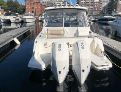 Powerboat with dual outboard motors docked in marina surrounded by buildings and other boats.