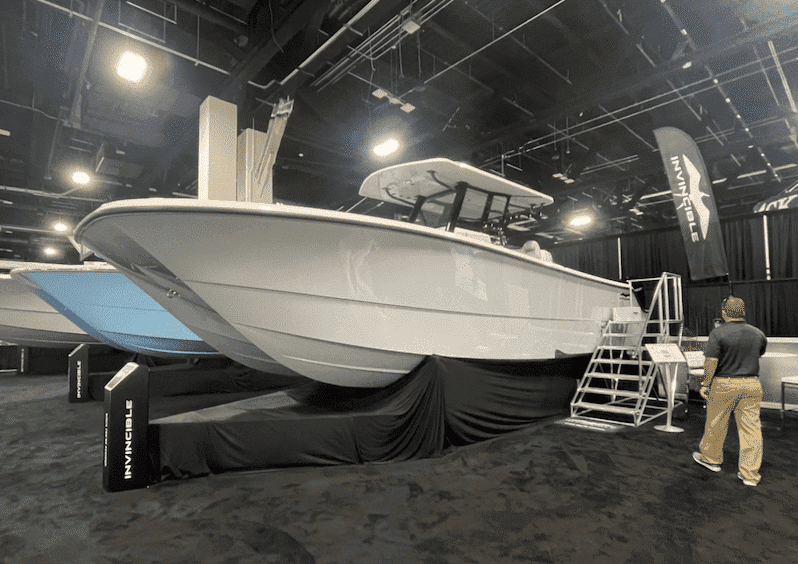 Sleek white powerboat on display in a showroom with a raised platform and branded banners.