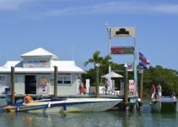 Powerboat fueling at a dockside marina, with gas prices displayed, offering essentials like bait and refreshments.
