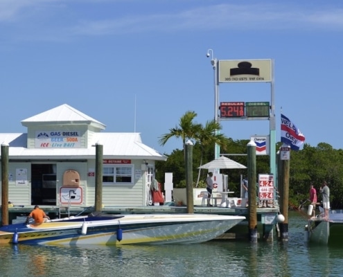 Powerboat fueling at a dockside marina, with gas prices displayed, offering essentials like bait and refreshments.