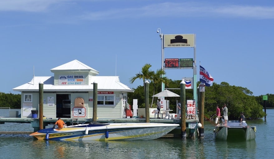 Powerboat fueling at a dockside marina, with gas prices displayed, offering essentials like bait and refreshments.