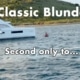 A catamaran near a coastal shoreline with Classic Blunder text overlay on a scenic boating day.